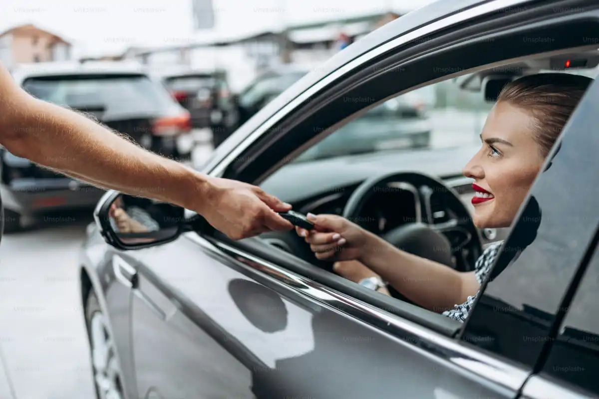 Satisfied and smiled female buyer sitting in her new car. She is smiling, looking at seller through open window while taking car keys from him.