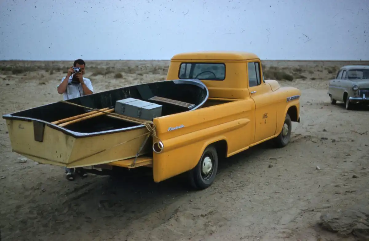 man in black jacket standing beside yellow single cab pickup truck during daytime