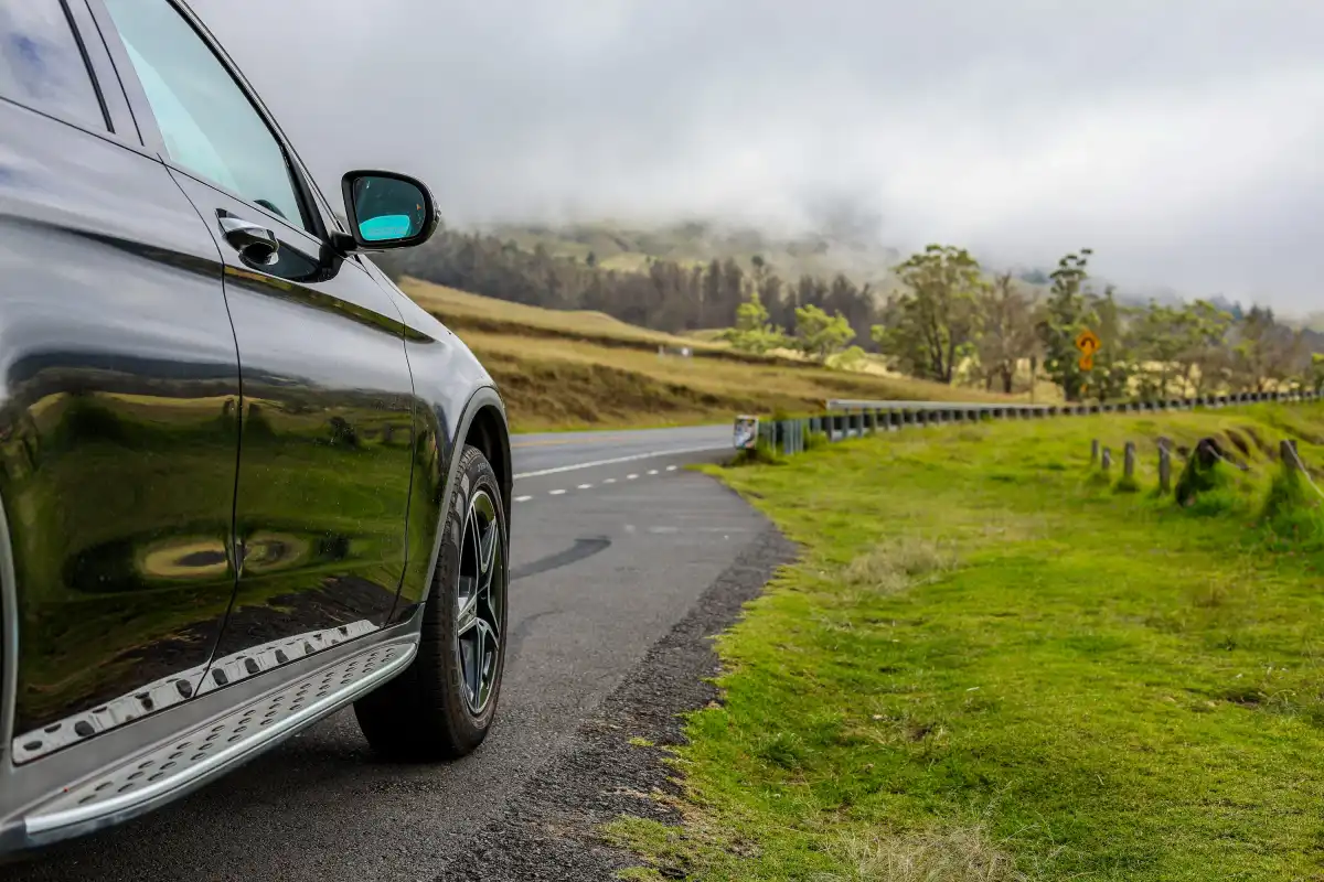 A black car driving down a road next to a lush green field